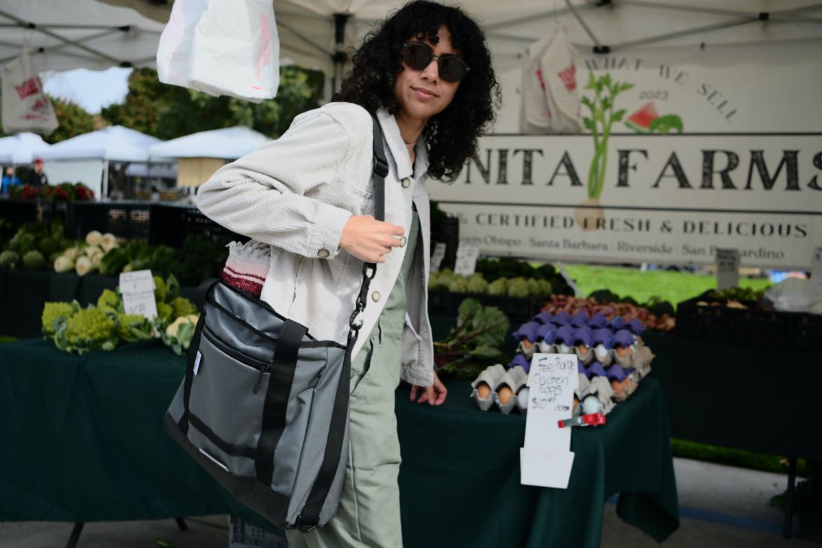 Woman with darky curly hair wearing sunglasses and a Road Runner Bags Everything Tote Bag at the farmers market