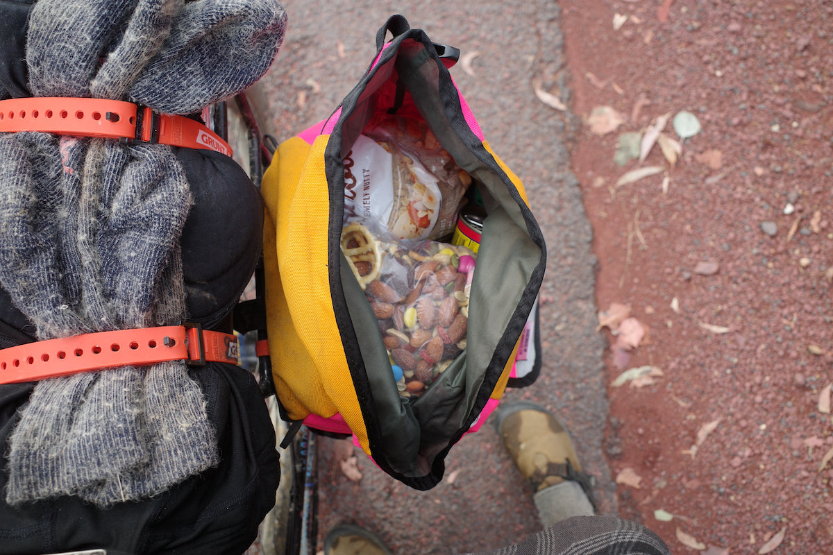 You are looking down into a loaded Bikepacking Pannier and seeing nuts, dried fruit, and other high-energy snacks. You can see the red clay beneath the bike, adding to the difficulty of the Hunt 1000.