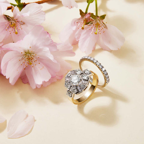 One engagement style diamond ring and one half eternity style diamond band cast in 14 kt yellow gold set among pink cherry blossom flowers.