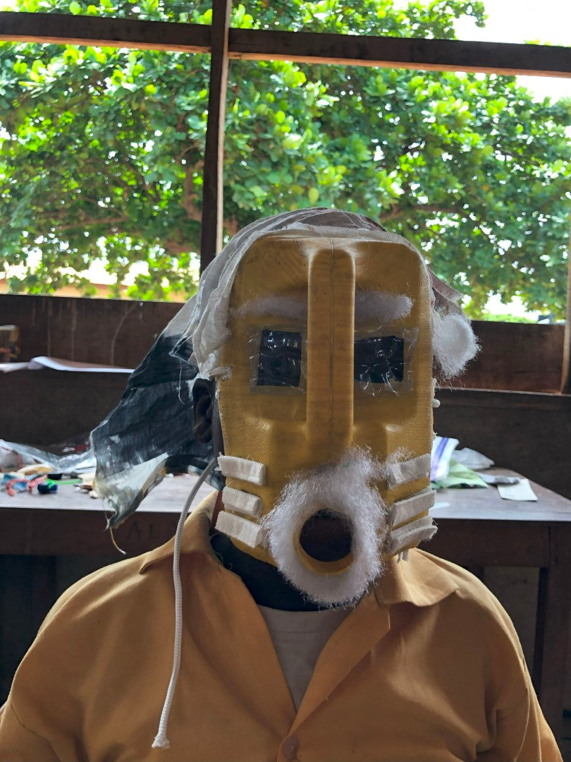 Cardboard mask with square eyes and cylindrical nose in a creative workshop setting.