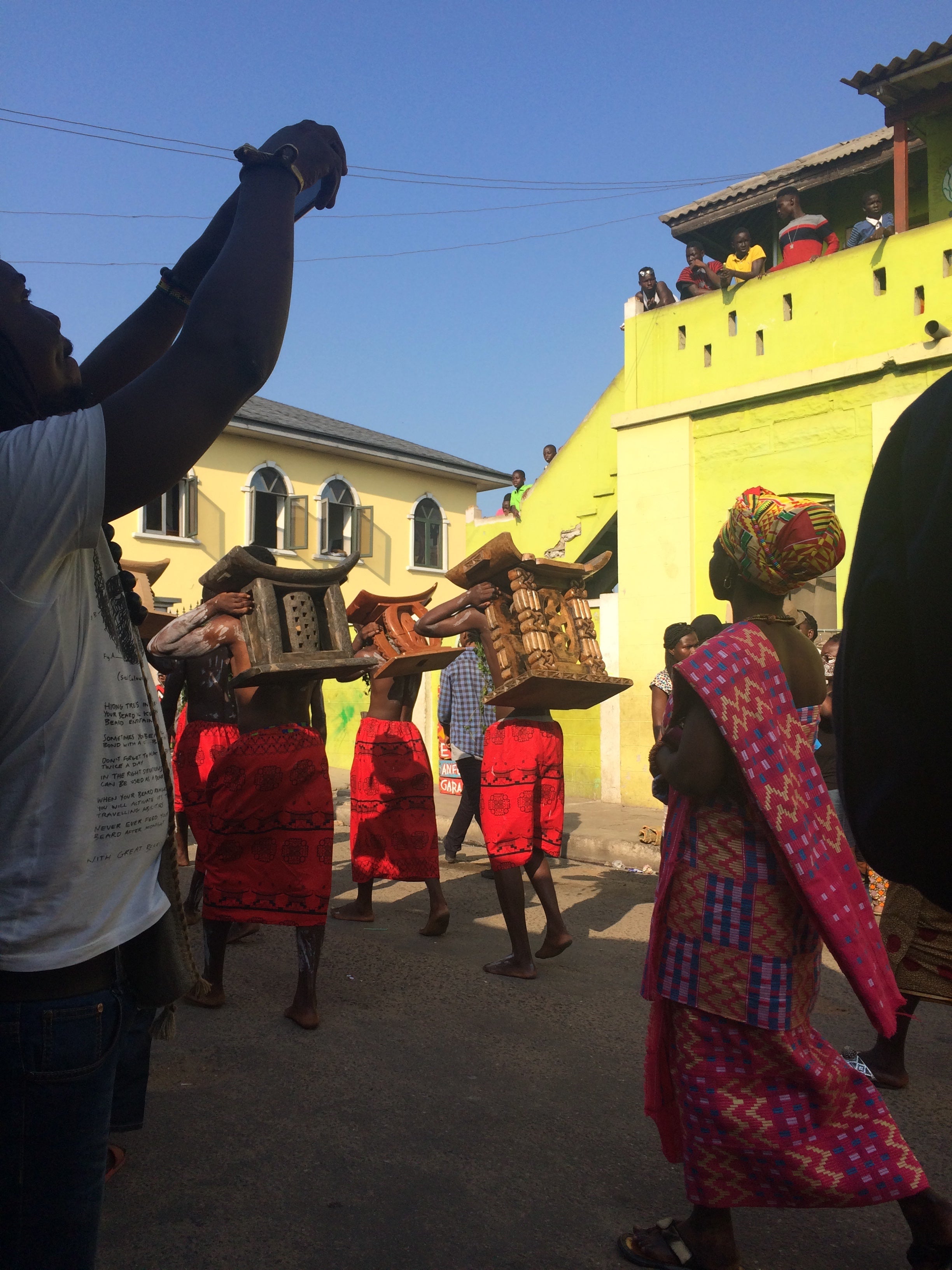 Group of people in red and black garments, some carrying objects on their heads, participating in a cultural procession.