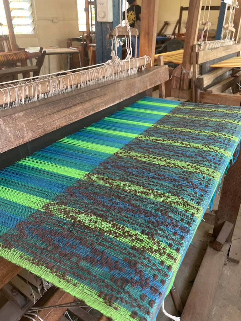 Traditional wooden weaving loom with blue and green striped textile, showcasing handweaving craftsmanship.