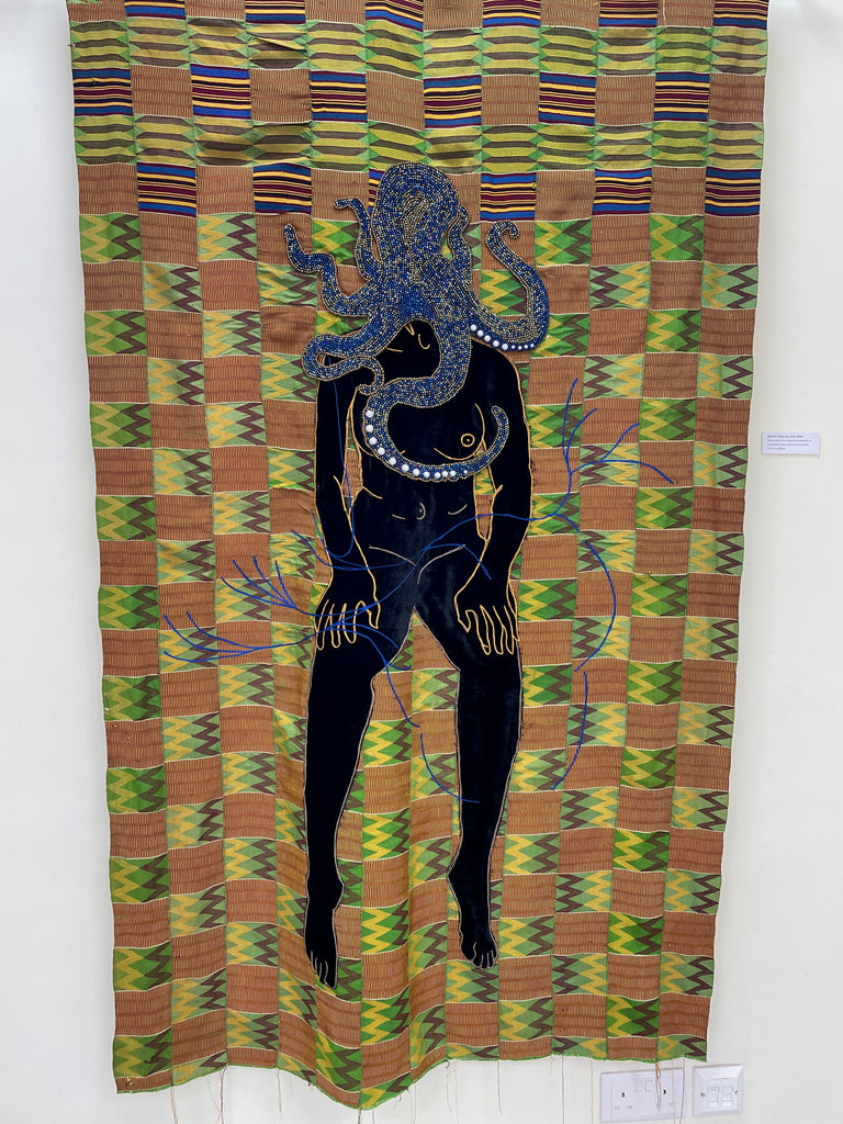 Textile artwork of octopus-human hybrid silhouette with white dots on patterned background.