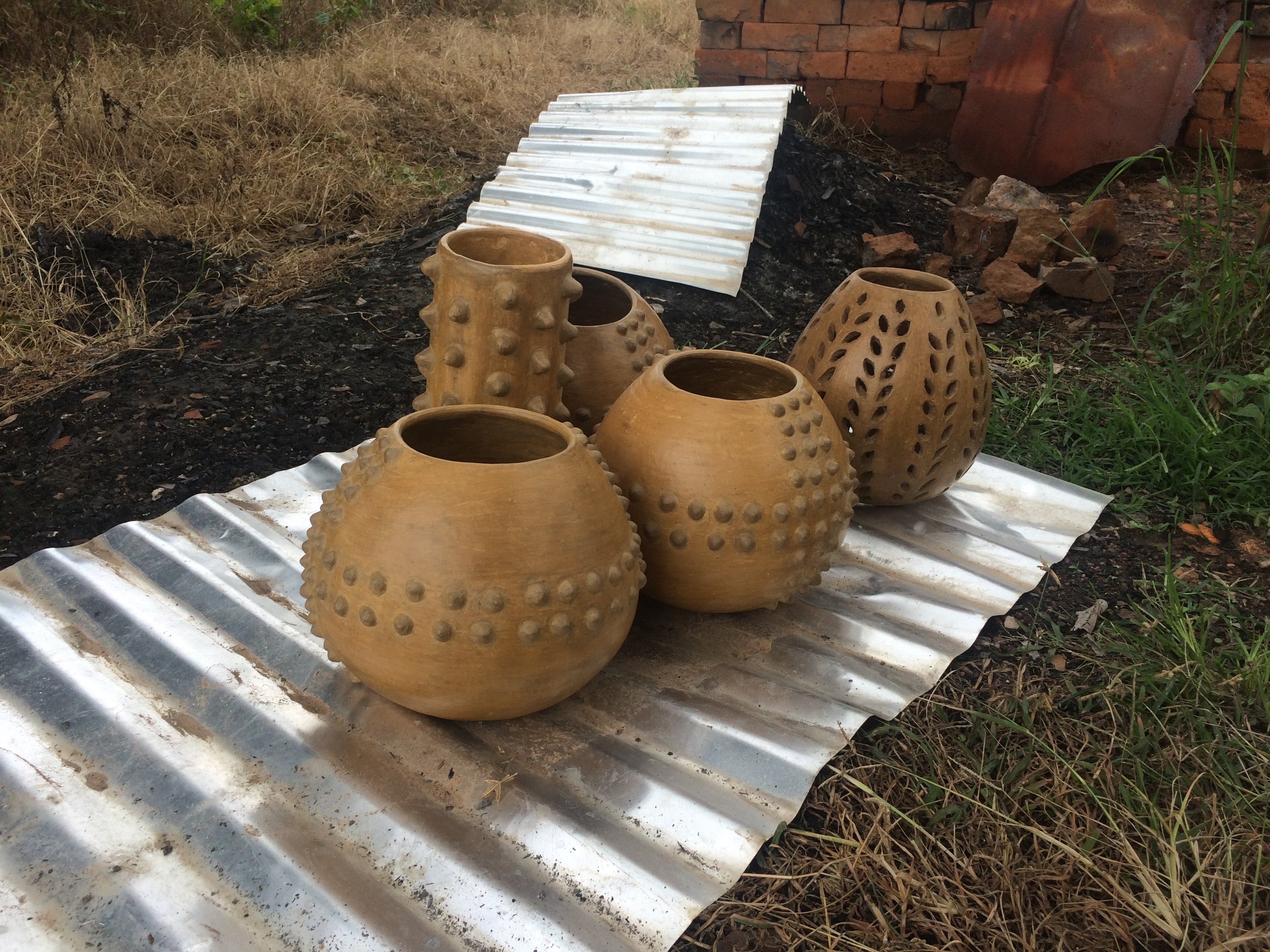Collection of five earthenware pots with various designs, displayed on a corrugated metal sheet at Kpando Potters Cooperative.