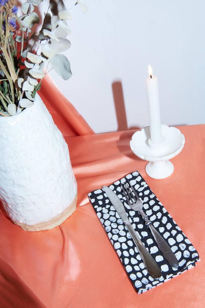 Modern table setting with eucalyptus, candle, and Osei-Duro fabric polka dot napkin, reflecting Osei-Duro’s repurposing of offcuts.