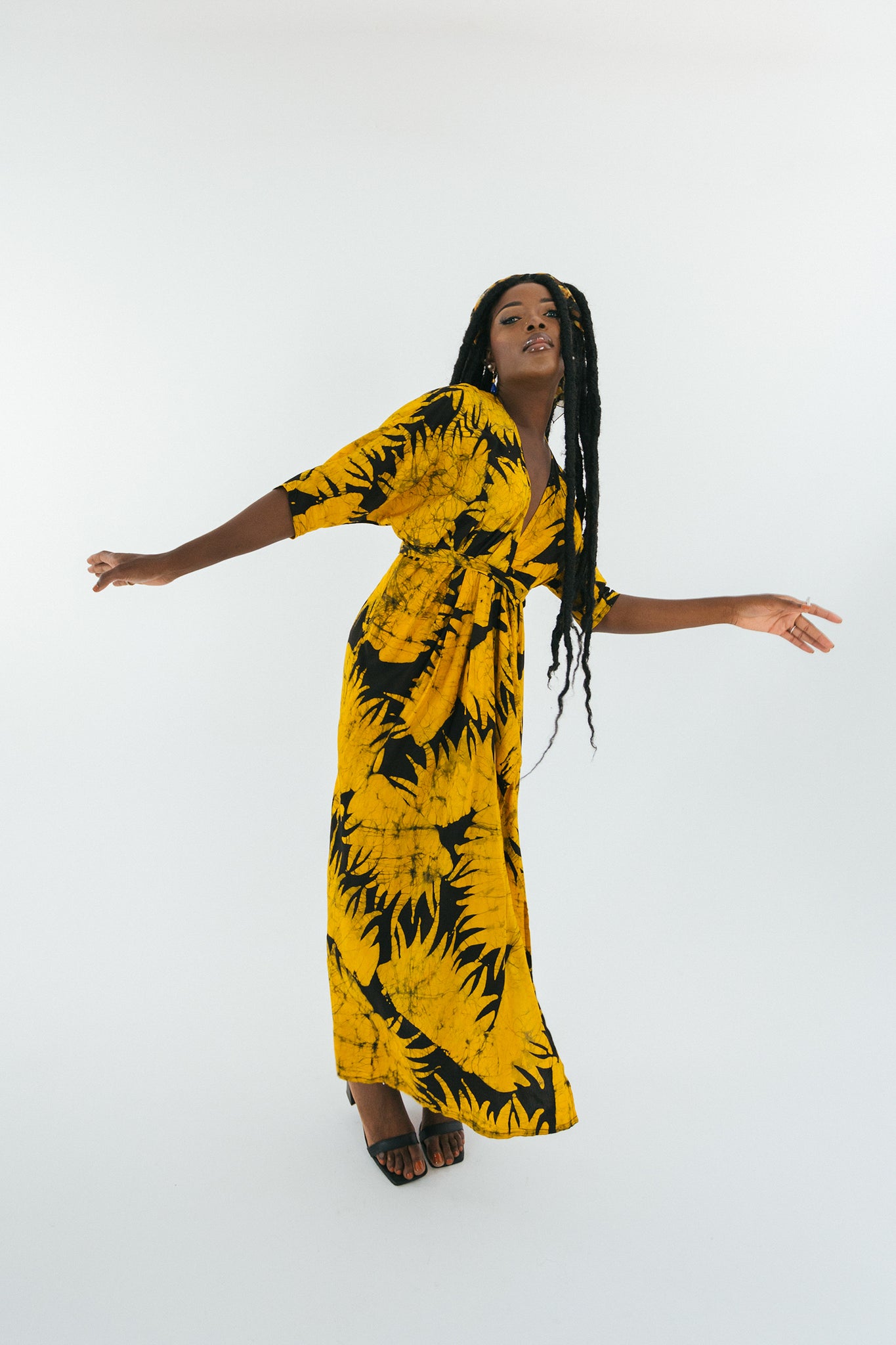 Vibrant yellow dress with black palm patterns captures Veso Golden’s dynamic pose, contrasting with a light backdrop.