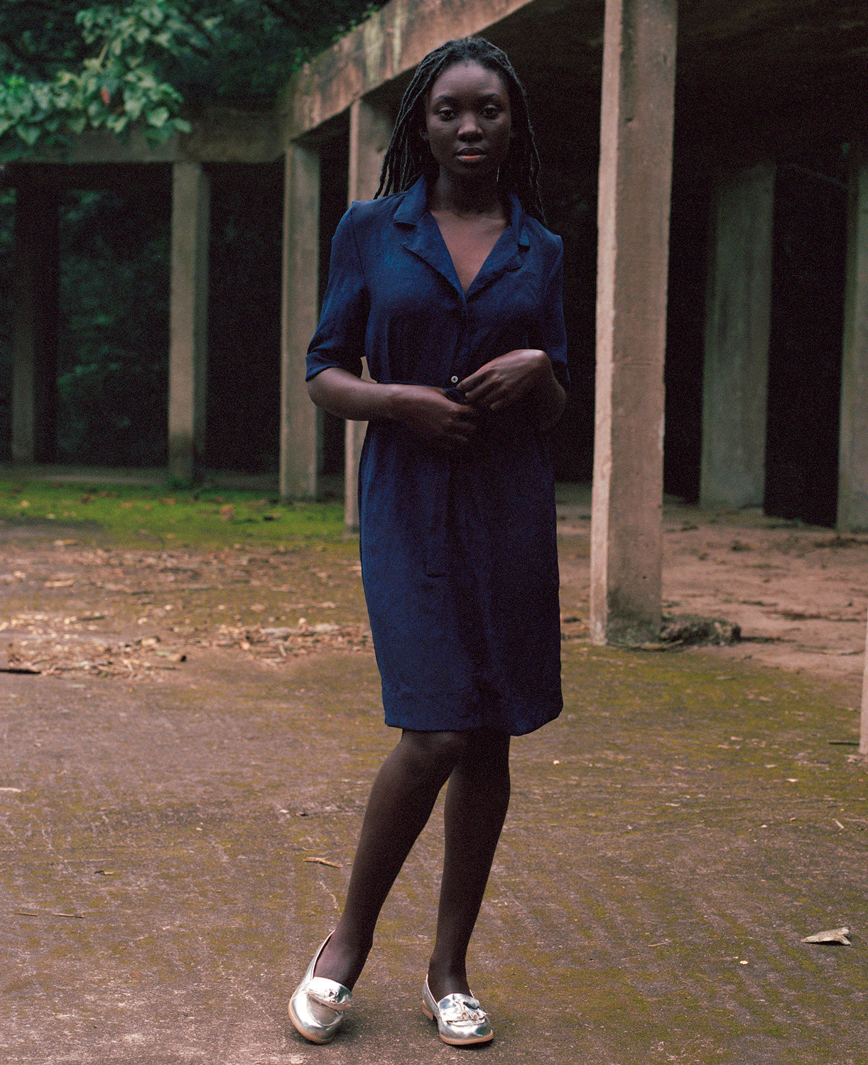 Person in a natural indigo Osei-Duro dress standing in front of concrete columns with greenery.