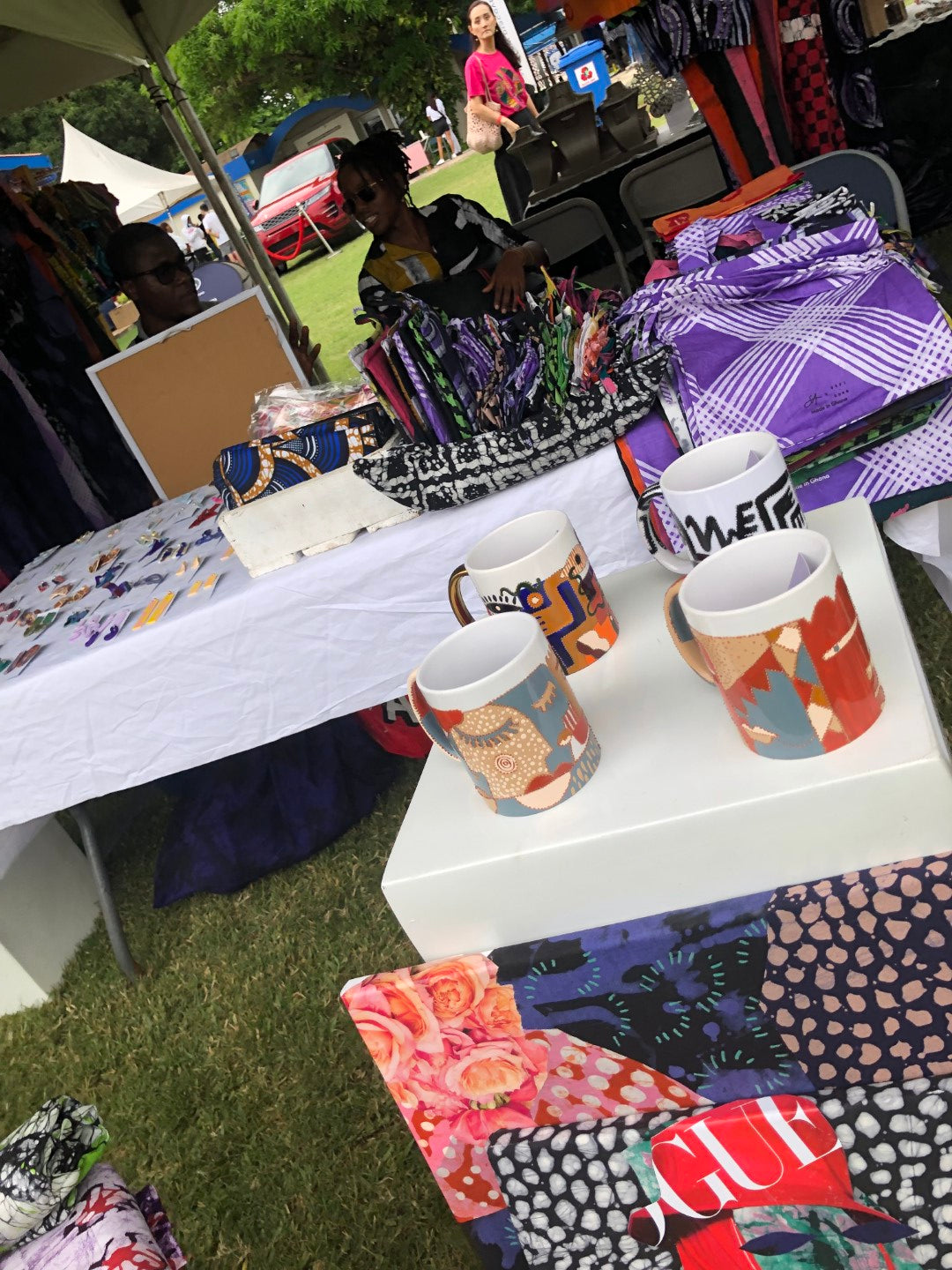 Colorful African print fabrics and designer mugs on display at an outdoor fair.
