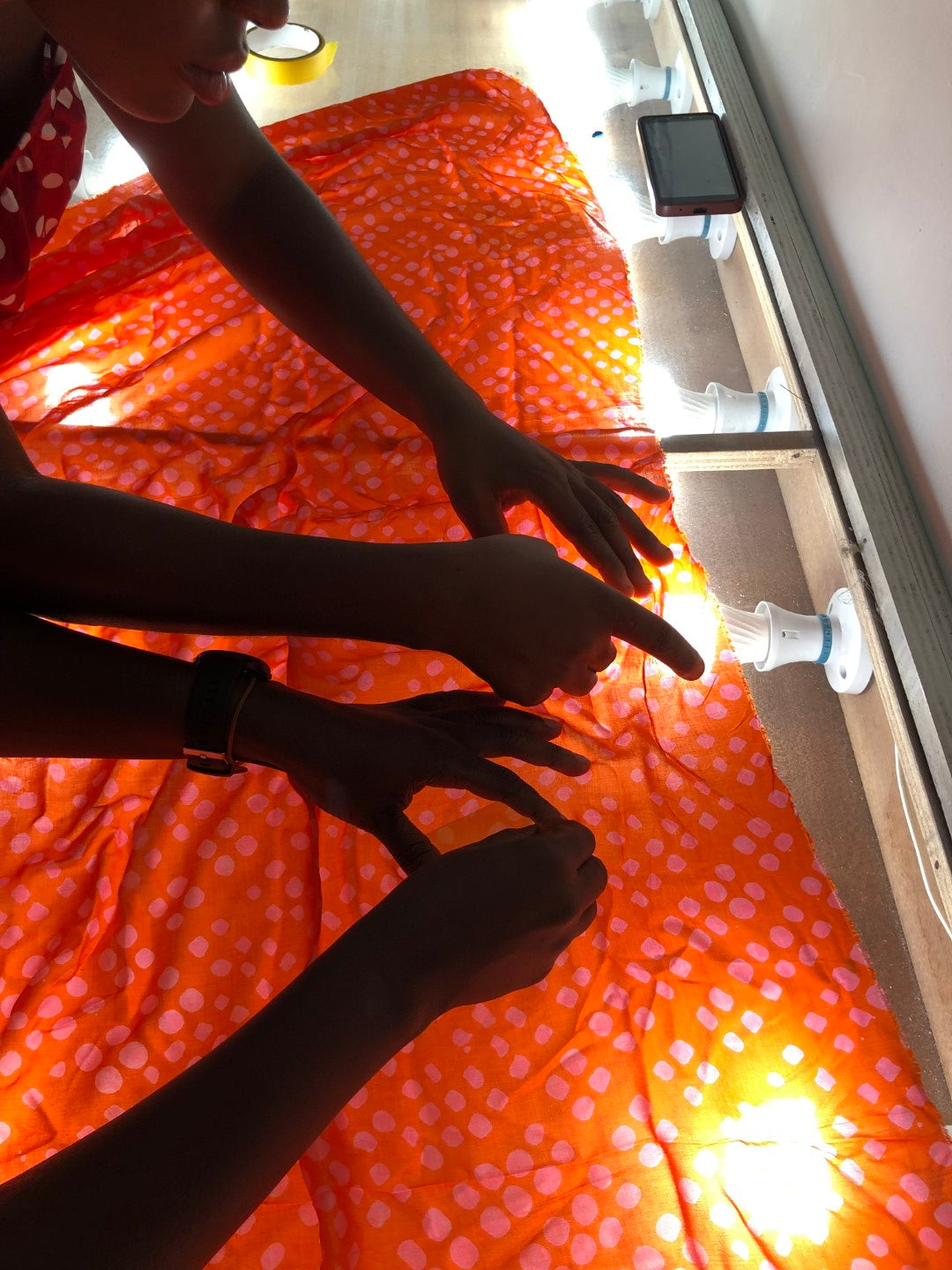 Two people checking orange fabric for damage on a light table.