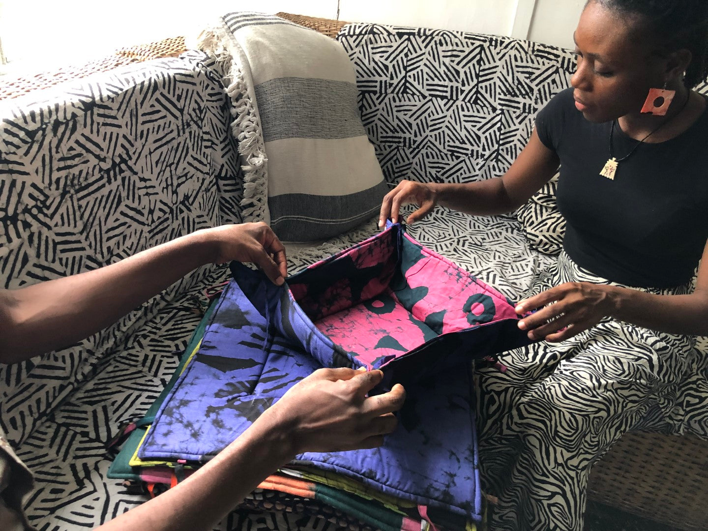 Two people reviewing vibrant batik dyed fabric on a patterned couch.