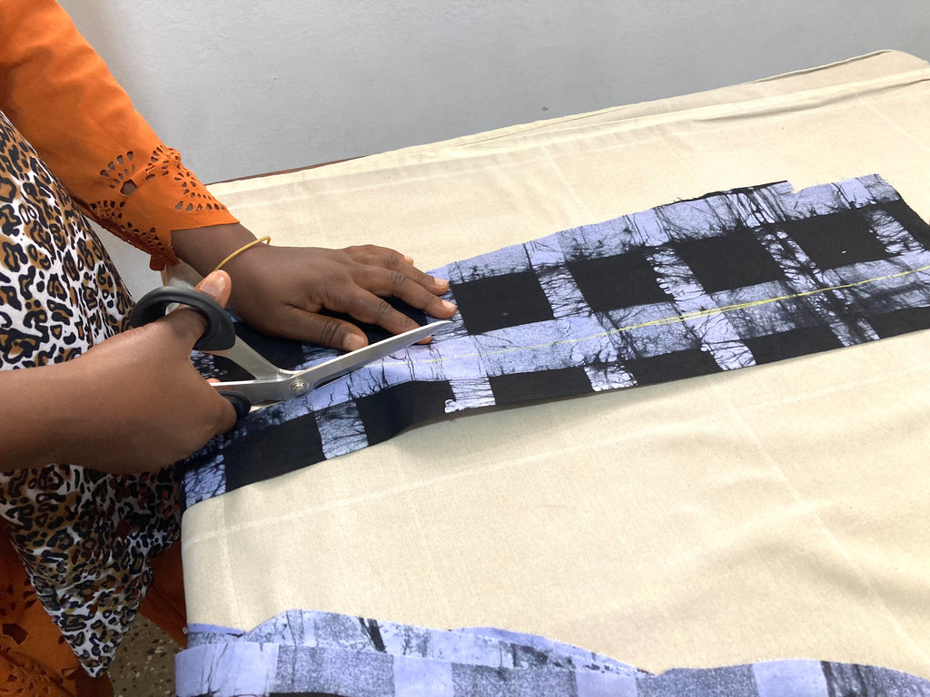 Hands meticulously cutting checkered fabric, showcasing Osei-Duro’s commitment to sustainable textile use and waste reduction.