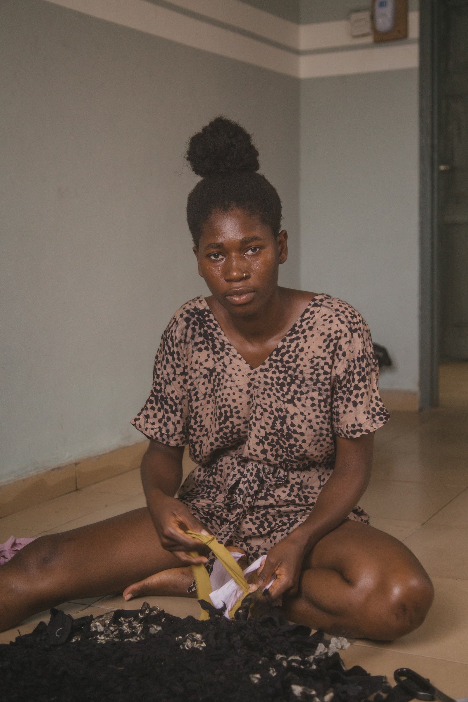 Woman sitting on the floor weaving black and yellow fabric strips.