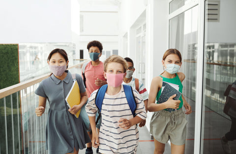 Kids in masks running through school hallway, carrying notebooks and backpacks