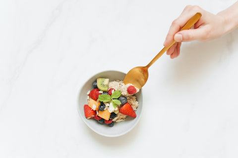 Oatmeal and fruit in ceramic bowl with a person holding a spoon