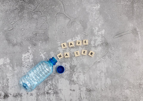 Plastic water bottle sitting on sand. Wooden letters spell out save water.