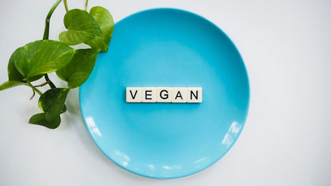 Scrabble tiles arranged on blue plate to spell vegan, surrounded by green leaves