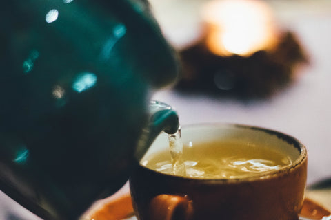 A photo of a ceramic tea pot pouring liquid into a glass tea cup