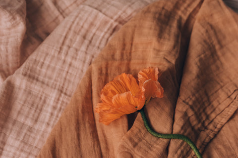 Orange and pink fabric sit beneath an orange flower with a green stem.