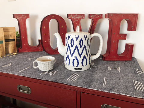 An electric tea kettle, a tea cup, and home decor that spells "Love" sits on top of a table. 