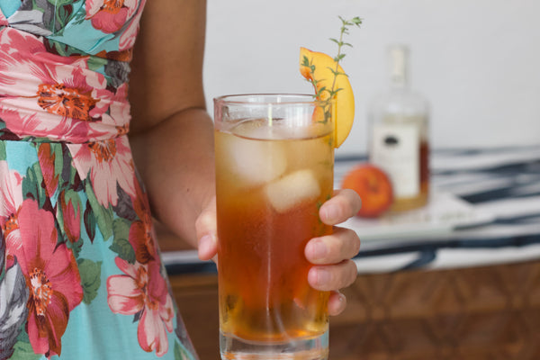 A person holds a glass of Summer Peach Rooibos cold brew made from Embrew's seasonal blend. 