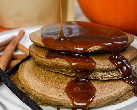 A plate of pancakes with maple syrup being poured on top. 