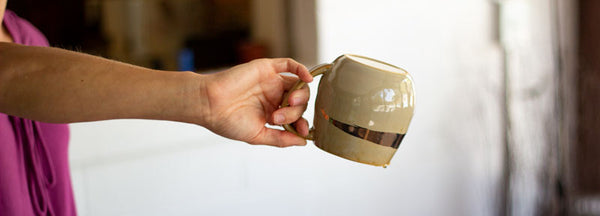 A gold mug being held upside down to dry out. 