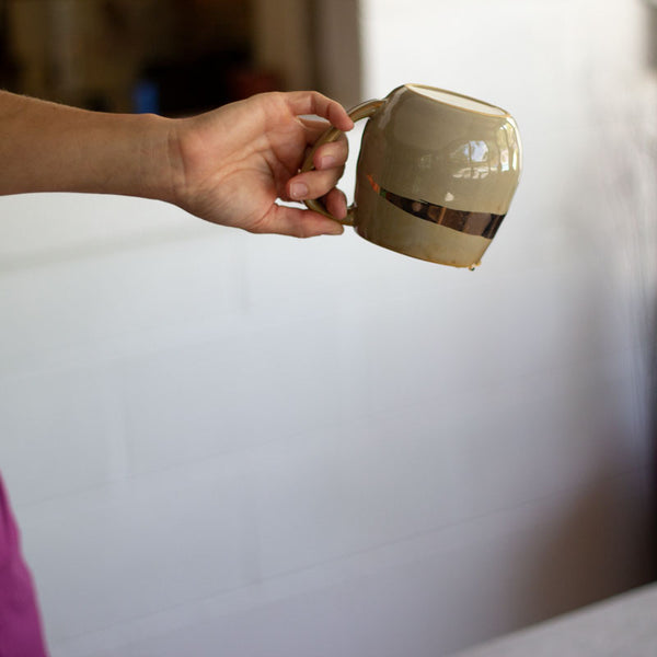 A gold mug being held upside down to dry out. 