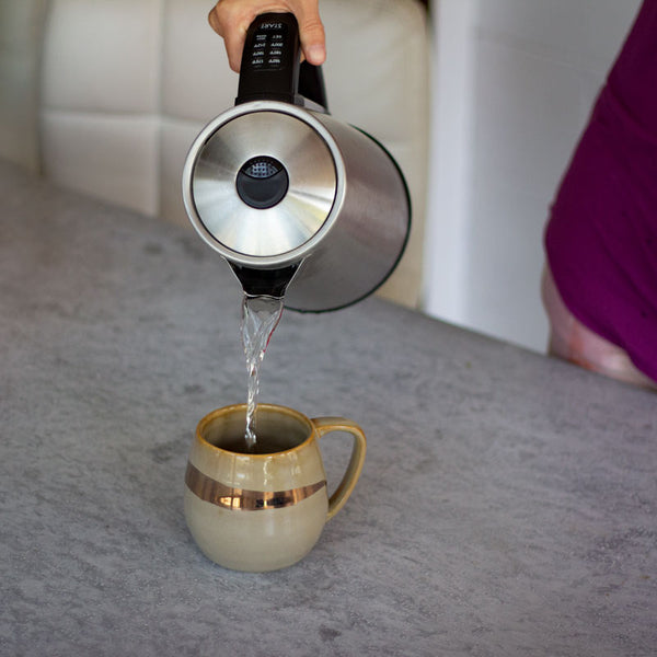 A person pours a hot cup of tea from an electric tea kettle. 