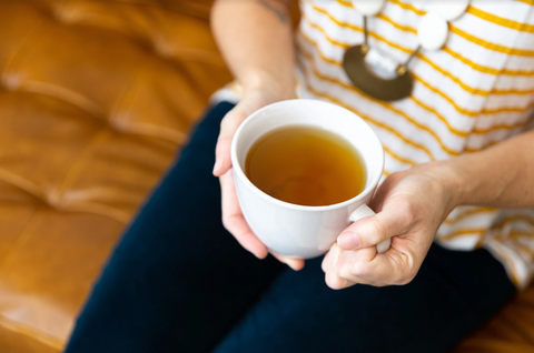 A woman holds a hot cup of tea in her lap. 