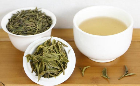 A cup of white tea sits beside two other cups fills with tea leaves. 