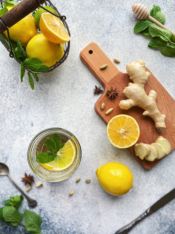 A cutting board with lemons and ginger beside a glass of iced tea. 