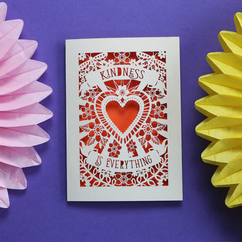 Beautiful papercut card showing a heart, flowers and butterflies. With "Kindness is everything" on banners above and below the heart. Cream card and orange background.