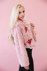 Model looks to camera wearing light pink fluffy faux fur coat with embellished heart motifs