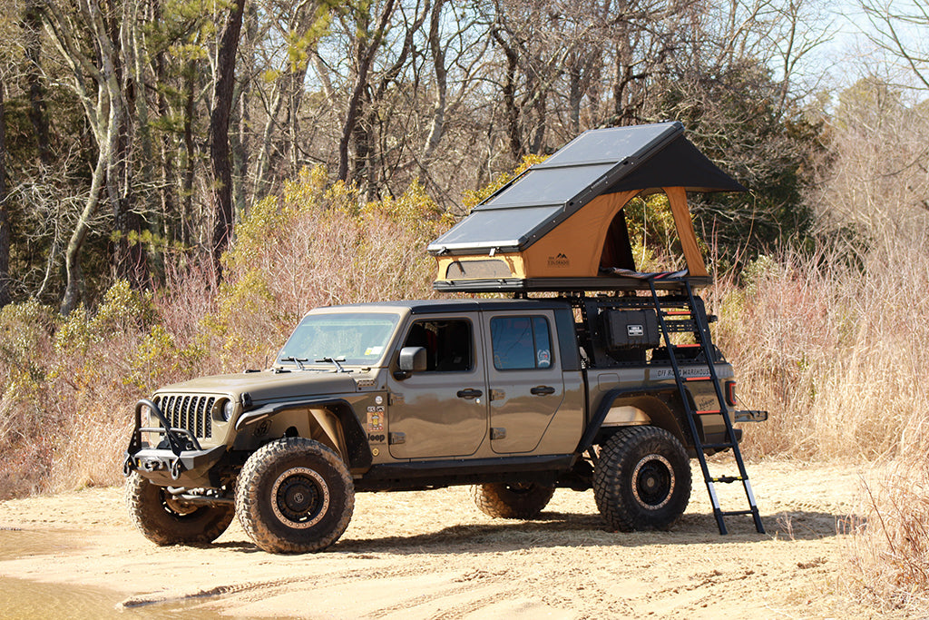 Gladiator with rooftop tent deployed on the sandy bank of a river