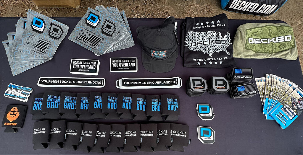 DECKED branded stickers, coozies, and clothing on a tabletop