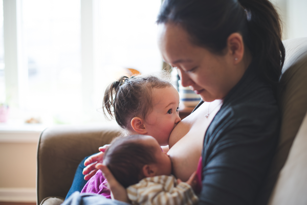 Baby girl and big sister breastfeeding at the same time