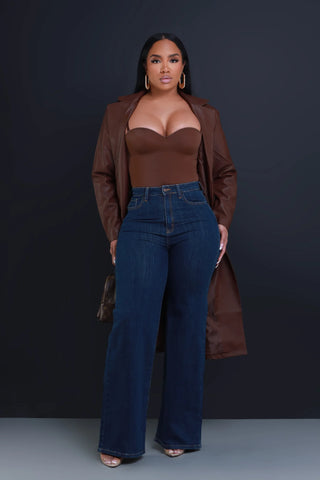 Swank girl wearing a paid of dark wash flare jeans with a brow top and leather trenchcoat