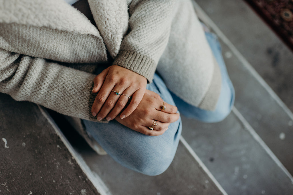 hands with rings on clasped on knee, wearing wild blue yonder jewelry