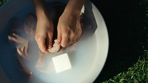 A pair of hands washing wool in a bowl of water with a bar of soap floating to the surface