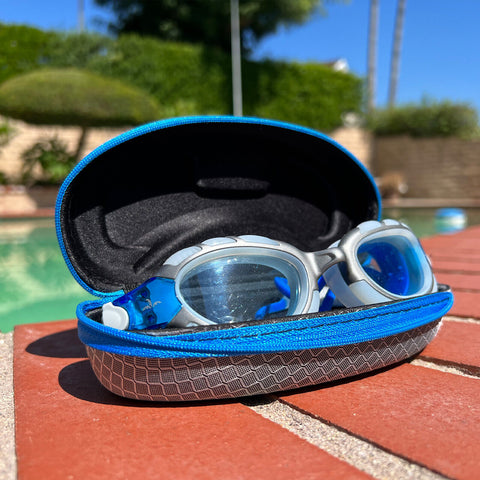Pair of swimming goggles inside a carrying case next to a swimming pool