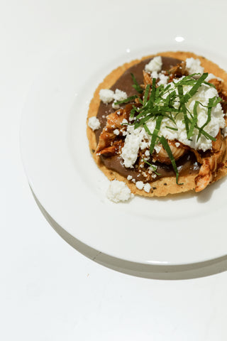 Tostadas de Tinga Poblana; mini homemade tostadas topped with refried pinto beans, chipotle stewed chicken, queso fresco crema and fresh epazote