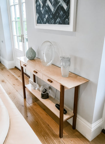 A console table with three drawers and a shelf displays a special collection of antique lalique glass in a modern living room.