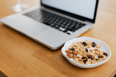 A plate of raisins and nuts next to a laptop.