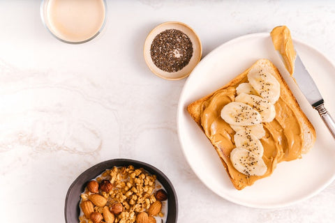 A plate with a piece of toast with peanut butter and banana slices on top.