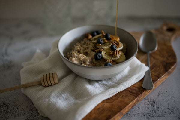 Honey pouring on a delicious oatmeal topped with blueberries, walnuts, and banana slices.