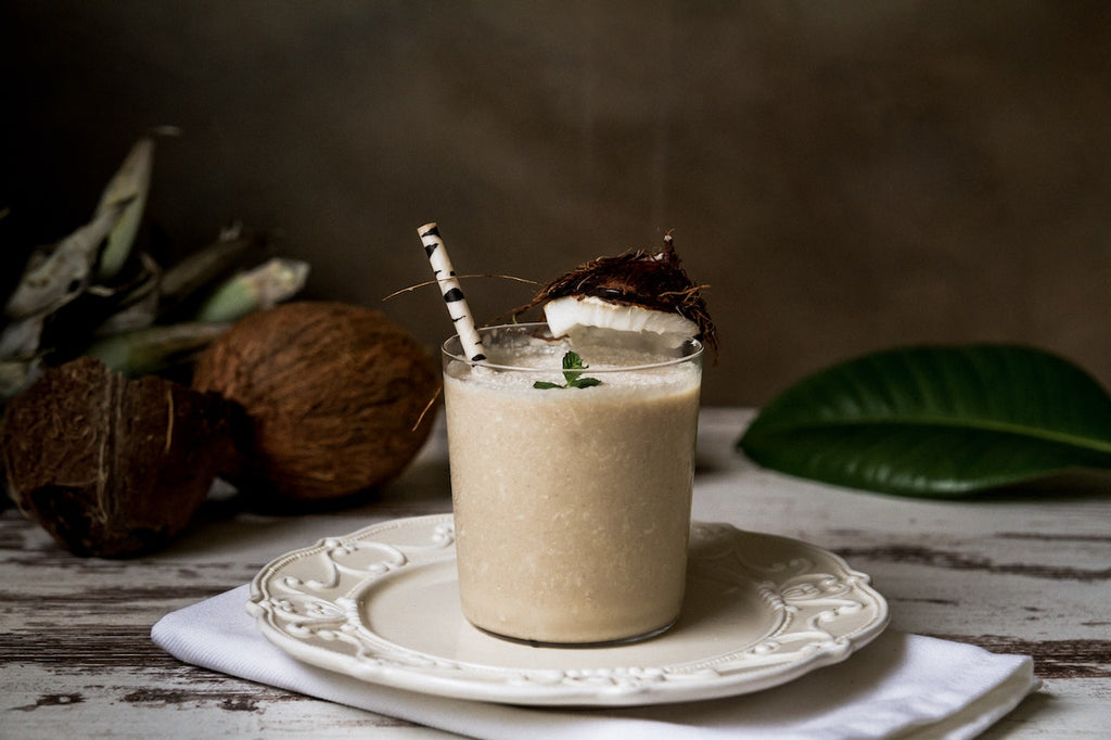 A thick, white protein shake with a slice of coconut placed on the rim of the glass.