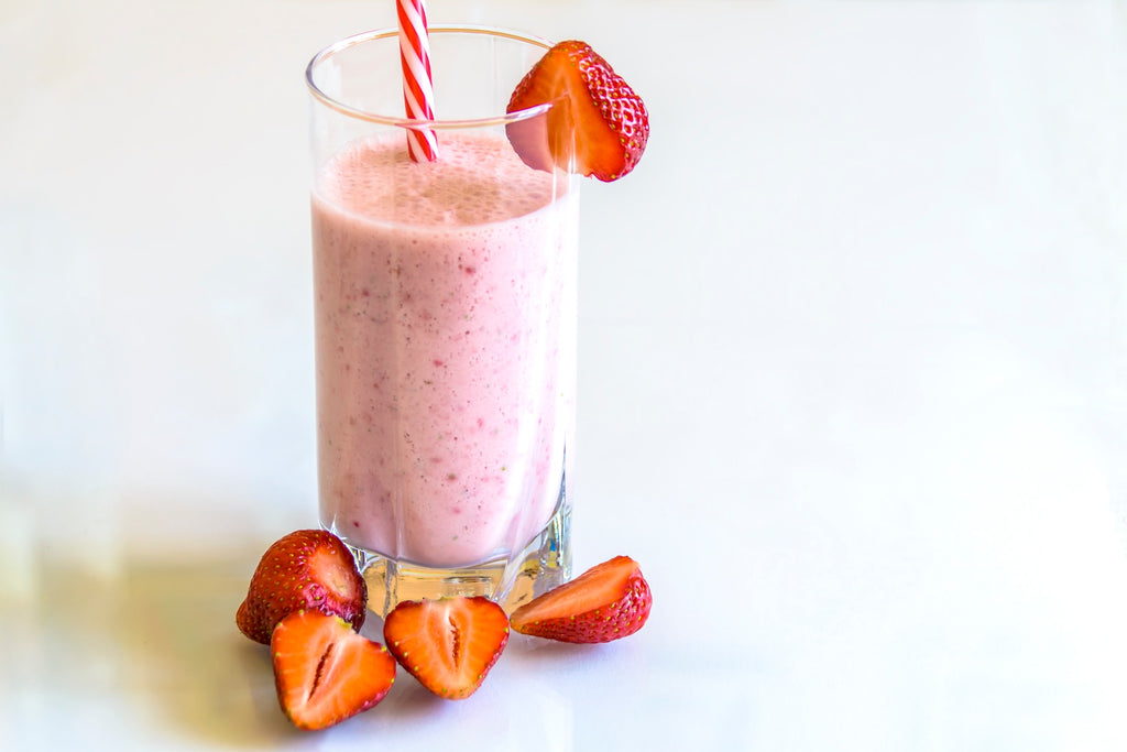 A strawberry protein shake with some sliced strawberries on the side.