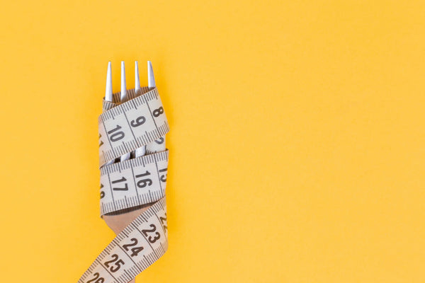 A fork wrapped with a measuring tape on a yellow background.