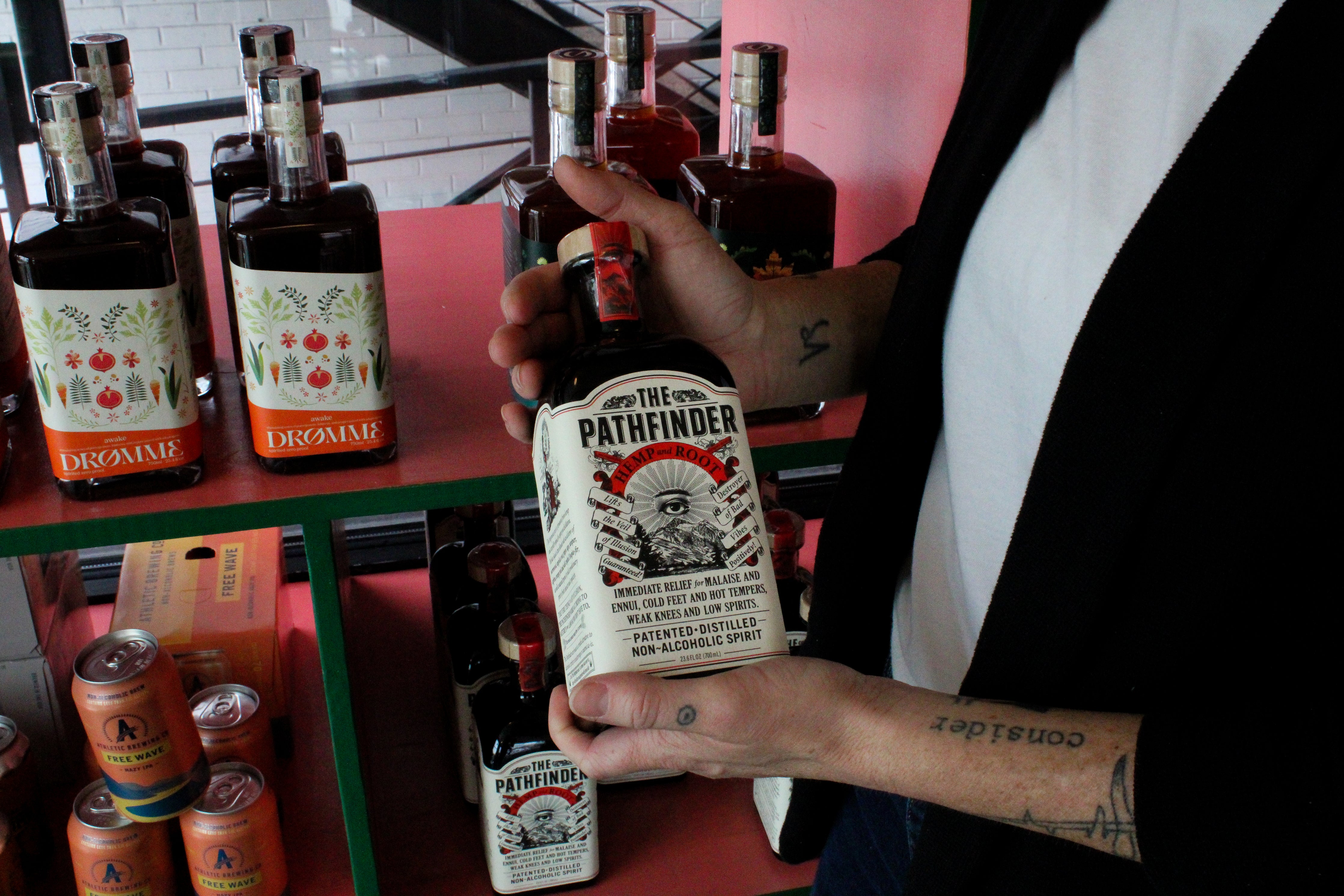 A woman holds an alcohol-free beverage in front of a bottle display at Curiosity.