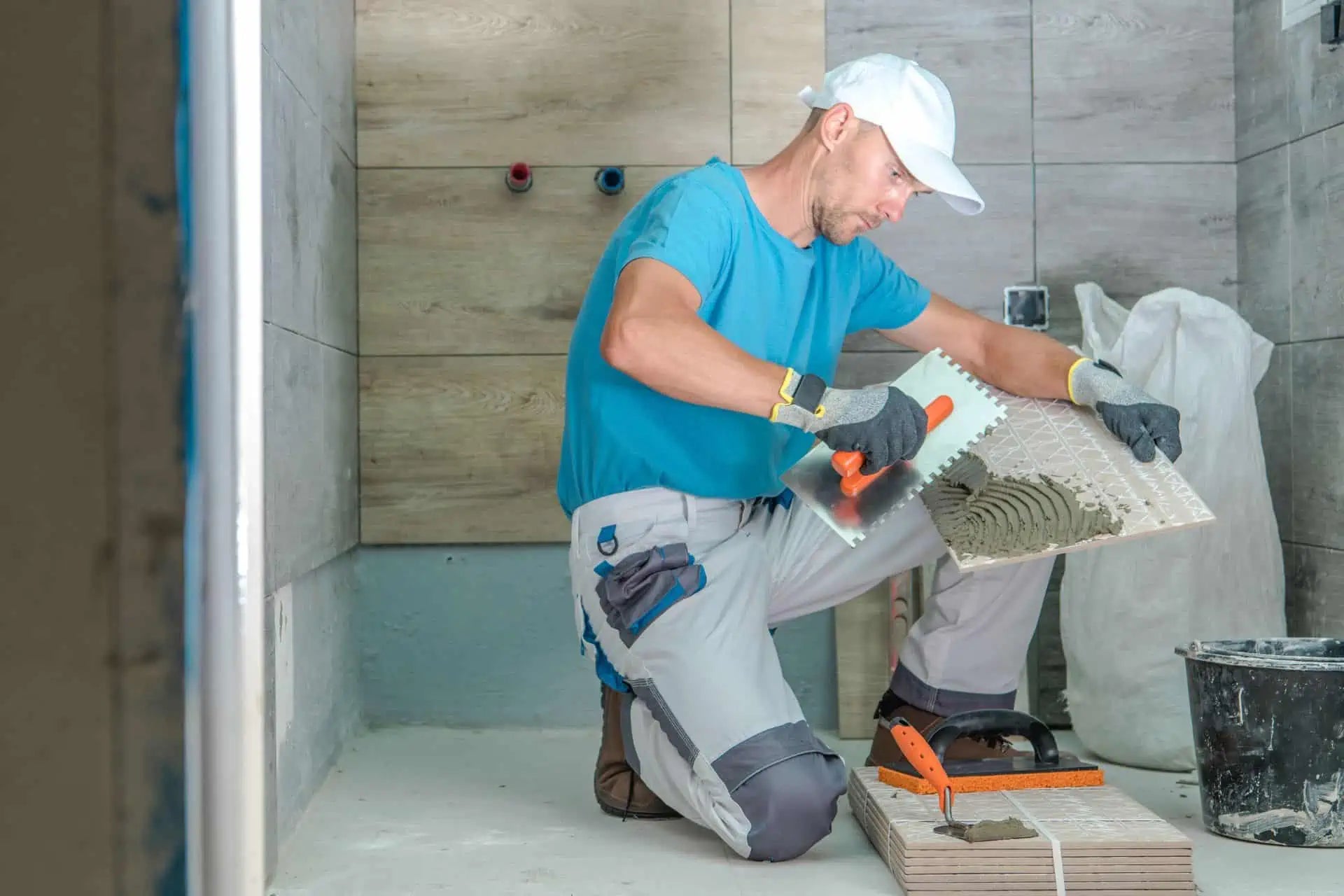 A man laying tiles on the concrete floor of a basement bathroom’s shower stall